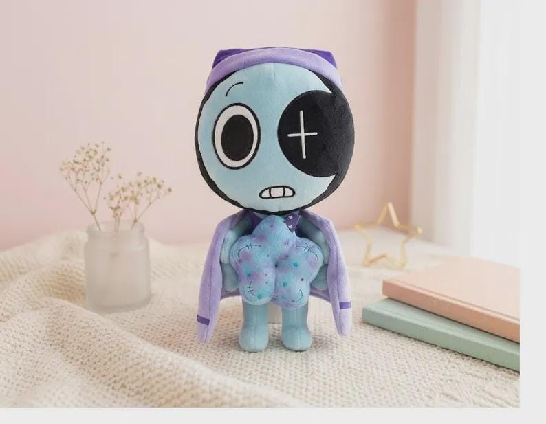 May include: A plush toy featuring a light blue, round head with one large white eye and one black eye patch with a white cross. It wears a purple cape and holds a light blue, star-shaped object with purple spots. The character has a small mouth.