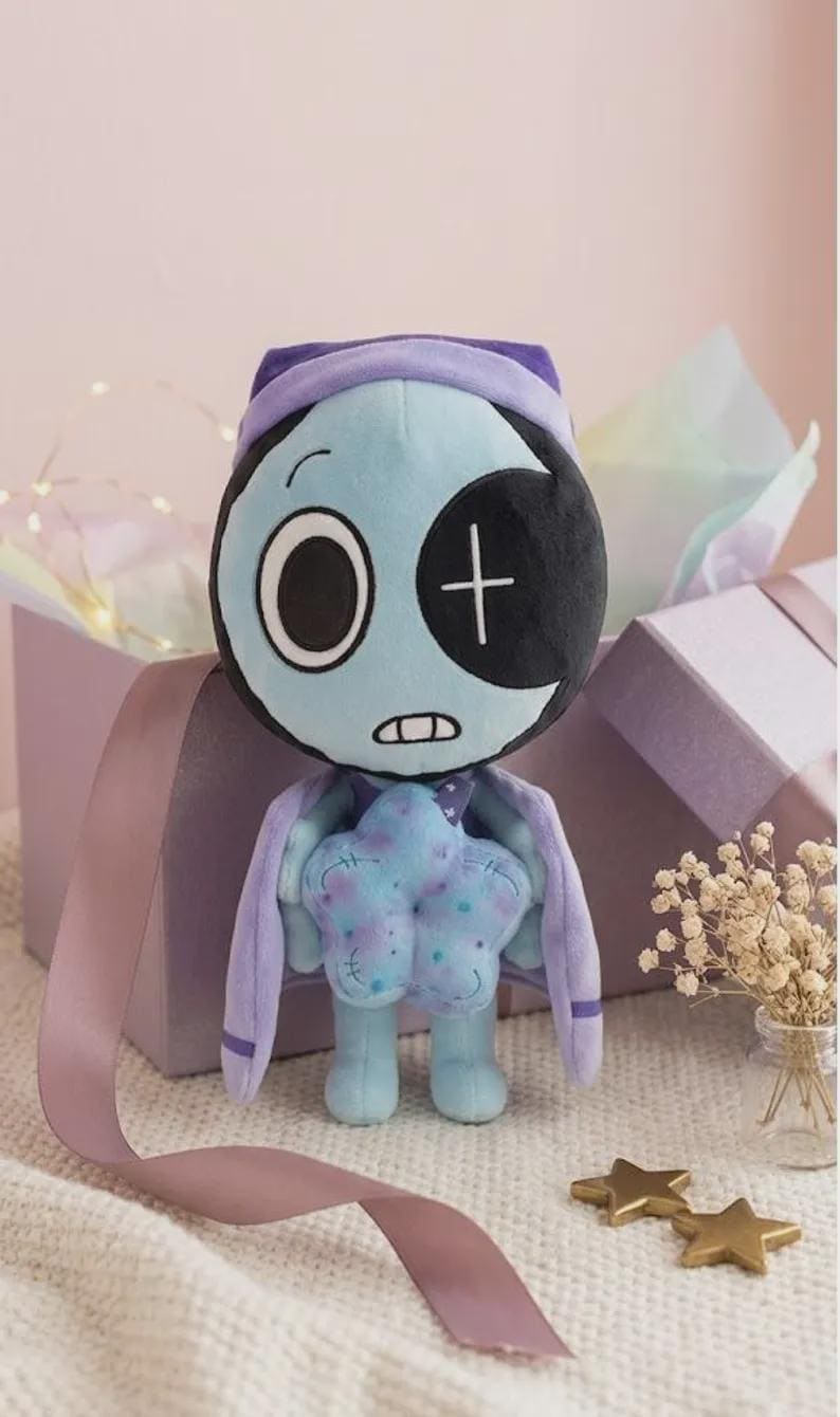 May include: A plush toy featuring a light blue, round head with one large white eye and one black eye patch marked with a white plus sign. The figure has a light blue body, a purple cape, and holds a textured, light blue star-shaped object in its hands.
