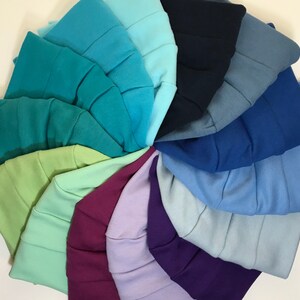 May include: A collection of colorful beanies arranged in a circular pattern. The beanies are displayed in a variety of shades, including teal, blue, purple, and green. Each beanie has a ribbed design.