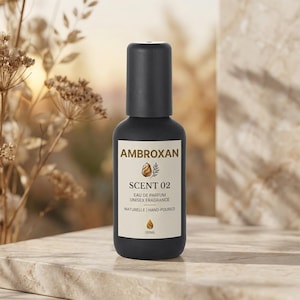 Może przedstawiać: Czarny flakon perfum z czarną nakrętką. Etykieta głosi "AMBROXAN Scent 02 Eau de Parfum Unisex Fragrance Naturelle Hand-poured 100ml". Tło przedstawia suszone rośliny.
