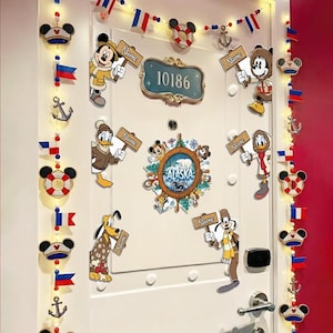 May include: A white door decorated with Disney character cutouts, including Mickey Mouse, Donald Duck, and Goofy, holding signs. The door also features a sign with the number 10186 and a decorative Alaska-themed emblem. String lights and nautical-themed garland complete the festive look.