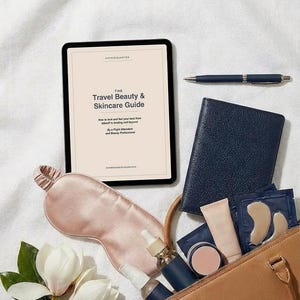 Peut inclure: Composition avec une tablette affichant "The Travel Beauty & Skincare Guide", un masque de sommeil rose, un carnet bleu marine, un stylo et un sac à main beige rempli de produits de beauté. Des fleurs de magnolia blanches et un flacon de sérum sont également présents.