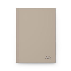 May include: A rectangular, taupe-coloured hardcover journal with a smooth, matte finish. The initials "AQ" are printed in dark grey in the lower right corner. The journal is new and unused, with a clean, minimalist design.