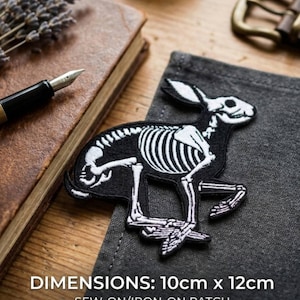 May include: A black and white sew-on/iron-on patch featuring a running rabbit skeleton design. The patch measures approximately 3.9 inches by 4.7 inches. The dimensions are printed on the patch. The patch is on a gray surface.