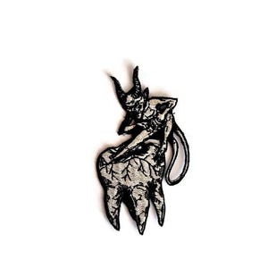 May include: Black and white embroidered patch featuring a devil figure seated on a tooth. The devil has horns and a tail. The tooth has three roots and a textured appearance. The patch is likely for clothing or accessories.