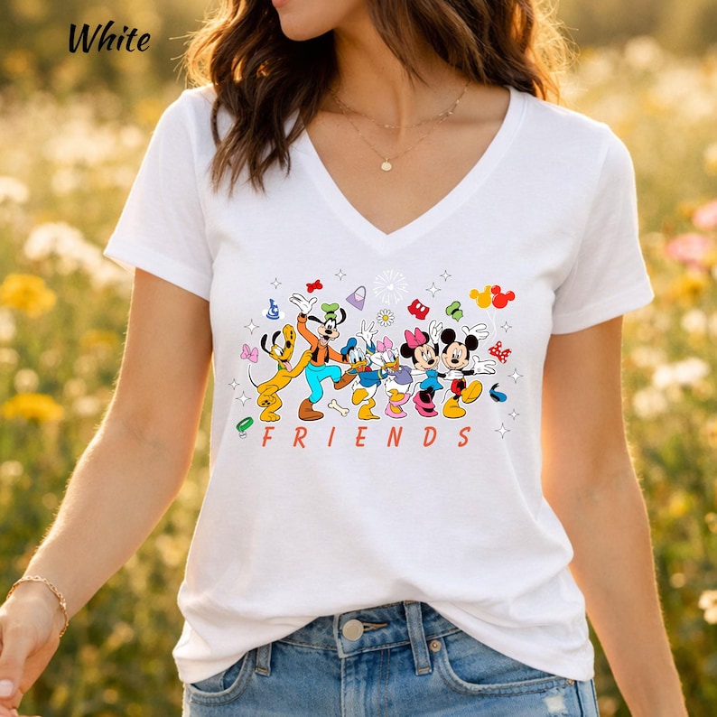 May include: A white V-neck t-shirt featuring a colorful graphic print of Pluto, Goofy, Donald Duck, Daisy Duck, Minnie Mouse, and Mickey Mouse standing together. The word FRIENDS is printed in red capital letters below the characters.