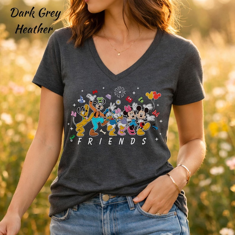 May include: A dark grey heather V-neck t-shirt featuring a graphic print of Disney characters including Pluto, Goofy, Donald Duck, Daisy Duck, Minnie Mouse, and Mickey Mouse. The word FRIENDS is printed in white below the colorful character illustration.