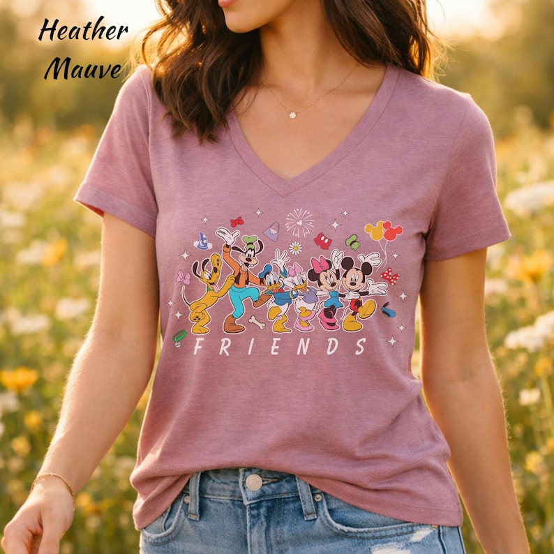 May include: A heather mauve V-neck t-shirt featuring a graphic print of Disney characters including Pluto, Goofy, Donald Duck, Daisy Duck, Minnie Mouse, and Mickey Mouse. The word FRIENDS is printed in white capital letters below the characters.