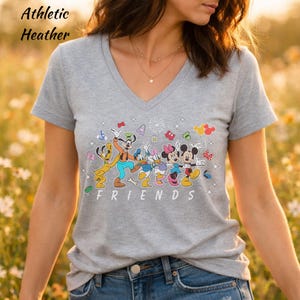 May include: An athletic heather gray V-neck t-shirt featuring a colorful graphic of Disney characters including Pluto, Goofy, Donald Duck, Daisy Duck, Minnie Mouse, and Mickey Mouse with the text FRIENDS printed in white below the characters.