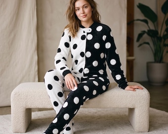 May include: A long-sleeved, footed one-piece pajama suit featuring a split design with a white base and black polka dots on one side, and a black base with white polka dots on the other. The garment has a round neckline and a snap closure.