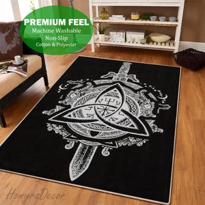 Pode incluir: Tapete retangular preto com um desenho de nó celta branco, uma espada e outros símbolos. O tapete tem uma borda branca e está sobre um chão de madeira. O tapete tem as palavras "Premium Feel", "Machine Washable", "Non-Slip" e "Cotton & Polyester".
