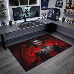 May include: A rectangular floor mat featuring a dark fantasy illustration of a horned, winged figure with pale skin and red accents. The mat has a black border and is positioned on a gray wood-look floor in a room with a gaming desk and computer setup.