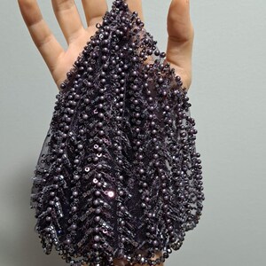 May include: A dark purple beaded evening bag with a wrist strap. The bag is covered in small, round beads and sequins, creating a textured, shimmering effect. The bag's shape is a rounded triangle.