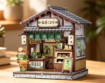 May include: A miniature model of a Japanese tea shop featuring a dark tiled roof, a wooden structure, and green fabric awnings with Japanese text. The shop includes white lanterns, a display case with small food items, and a sign reading Matcha.