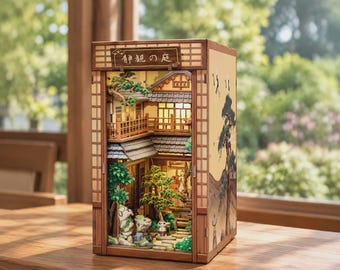 May include: A wooden miniature diorama box featuring a Japanese-style building with interior lighting, green trees, and stone paths. The top sign displays the Japanese text 静観の庭. The exterior side panel features a black ink-style illustration of a tree.