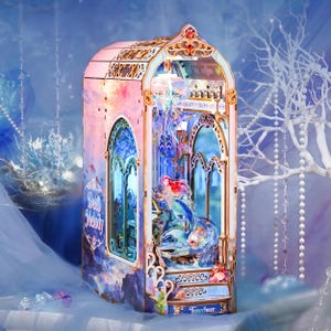 Può includere: Un diorama in legno intitolato Deep Melody che raffigura una scena sottomarina con una sirena, una luce a forma di medusa e finestre ad arco. La struttura è decorata con sfumature rosa e blu, intagli ornamentali e il testo Tonecheer.