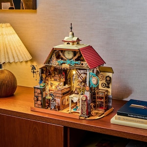 May include: A miniature wooden clock shop model featuring a red roof, a central clock face, and intricate interior details including a workbench, shelves, and various timepieces. The structure is illuminated by internal lights and displays a detailed facade.