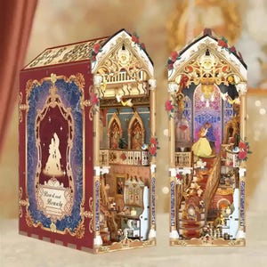 May include: A book-shaped diorama kit featuring a red and gold exterior with the text Beast and Beauty. The interior displays a multi-level castle scene with a staircase, a ballroom, and miniature figures of a couple dancing under a chandelier.