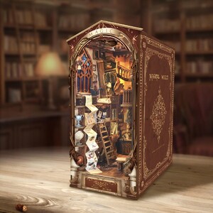 May include: A brown book-shaped diorama titled Magical World featuring an interior scene of a library with a wooden ladder, a long scroll, a globe, and a window. The exterior cover has gold filigree patterns and the text Magical World printed on it.