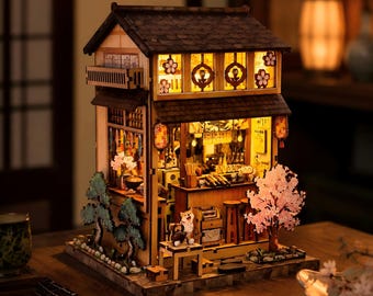 May include: A miniature wooden model of a Japanese-style tavern featuring a dark tiled roof, warm interior lighting, a small bar with stools, a Shiba Inu figure, and decorative cherry blossom trees on the exterior, all crafted with intricate detail.