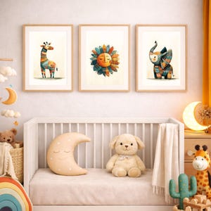 Puede incluir: Tres impresiones en acuarela enmarcadas que representan una jirafa, un sol y un elefante con patrones coloridos. Se exhiben sobre una cuna blanca con una almohada de media luna y un perro de peluche. La habitación tiene un ambiente cálido.