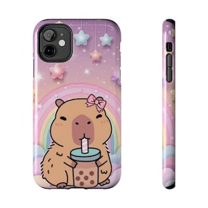 May include: A phone case featuring a cartoon capybara with a pink bow, drinking boba tea. The case has a pastel rainbow and star design. The case is shown from the front and side.