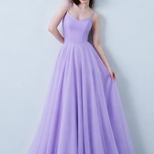 Puede incluir: Un vestido largo de color lavanda con un corpiño ajustado, escote corazón y tirantes finos. La falda está confeccionada con varias capas de tul transparente, creando una silueta amplia y fluida que llega hasta el suelo.