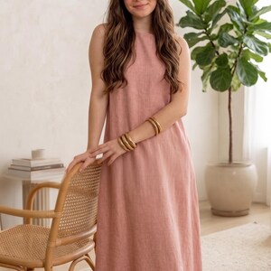 Puede incluir: Un vestido largo sin mangas de color rosa empolvado. La prenda presenta un cuello alto y redondeado con una silueta recta y relajada que llega hasta los tobillos. El tejido muestra un acabado texturizado y de aspecto tejido.