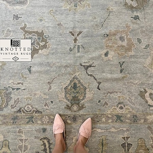 May include: A light blue area rug featuring a faded, multi-coloured floral and geometric pattern in shades of tan, grey, and muted green. A rectangular logo in the corner displays the text KNOTTED VINTAGE RUGS with a small graphic icon.