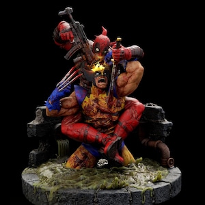 May include: A detailed collectible statue featuring Deadpool in a red and black suit holding a rifle and sword, positioned behind Wolverine in a yellow and blue suit with extended metal claws. Both figures appear battle-worn with visible damage.