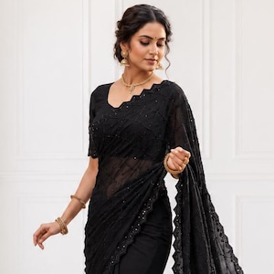 May include: A black saree with intricate embroidery and a sheer, embellished border. The saree features a matching blouse with short sleeves and a delicate neckline. The fabric drapes elegantly, showcasing the detailed design.