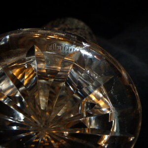 May include: Close-up of a clear glass crystal decanter base with a cut glass pattern. The base has a circular shape and a textured surface.