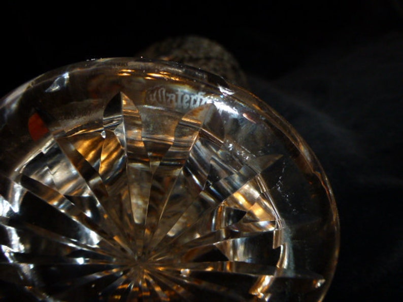 May include: Close-up of a clear glass crystal decanter base with a cut glass pattern. The base has a circular shape and a textured surface.