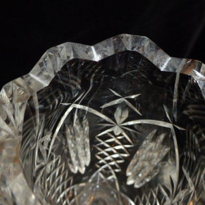 May include: A clear glass vase with a cut glass design. The vase has a scalloped rim and a floral pattern.