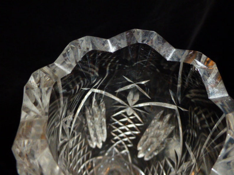 May include: A clear glass vase with a cut glass design. The vase has a scalloped rim and a floral pattern.