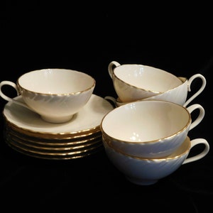May include: A set of six white teacups and saucers with gold trim. The cups and saucers are stacked on top of each other.