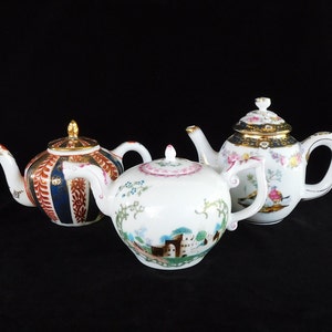 May include: Three ornate teapots with detailed patterns. The teapots showcase floral, striped, and landscape designs. They are white with gold trim and vibrant colours. The teapots are presented against a black backdrop, highlighting their intricate craftsmanship.