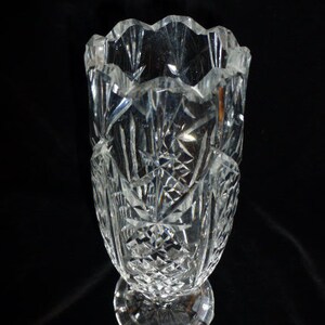 May include: A clear glass vase with a cut crystal design. The vase has a wide mouth and a narrow base.
