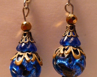 Könnte beinhalten: Ein Paar blaue und goldene Ohrringe mit einem tropfenförmigen Kristall-Anhänger. Die Ohrringe haben eine blaue Glasperle mit goldenen Akzenten und einem filigranen Design.