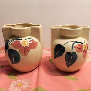 May include: Two vintage ceramic vases with a cream-colored background and floral designs in shades of pink, yellow, blue, and green.