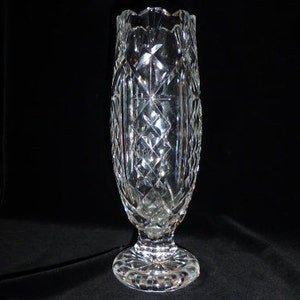 May include: A clear glass vase with a cut crystal design. The vase has a tall, slender body and a wide, flared base.