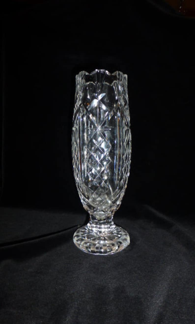 May include: A clear glass vase with a cut crystal design. The vase has a tall, slender body and a wide, flared base.