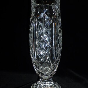 May include: A clear glass vase with a cut crystal design. The vase has a tall, slender body and a wide, flared base.