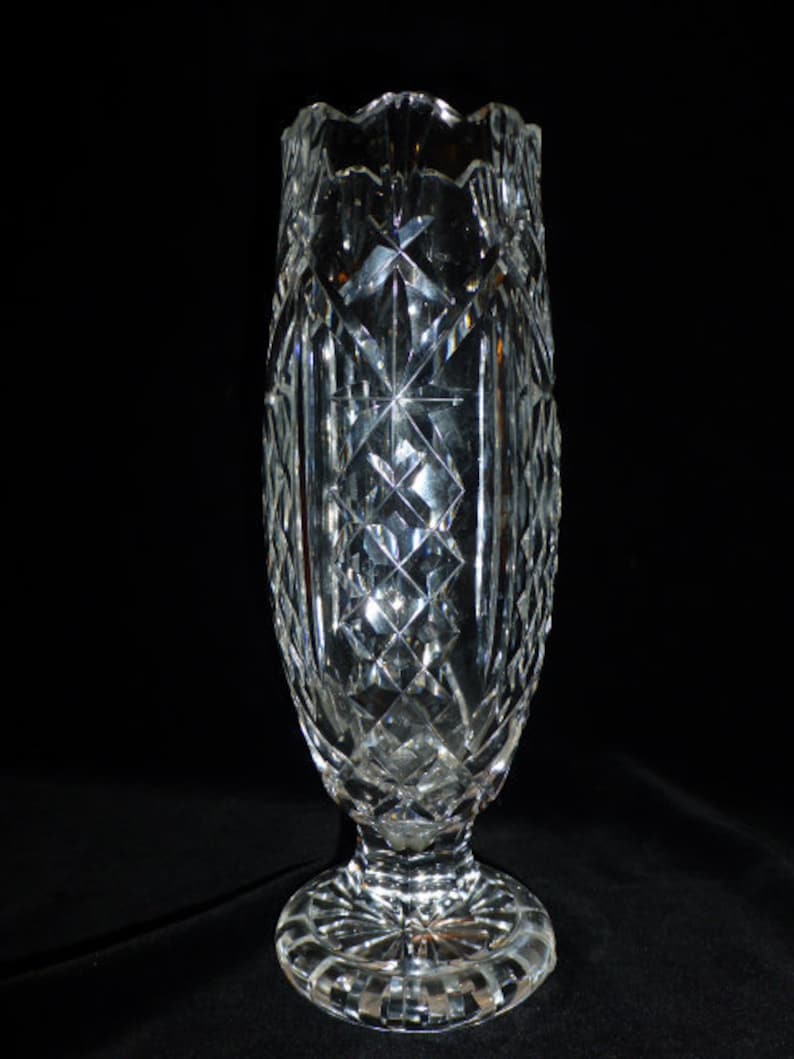 May include: A clear glass vase with a cut crystal design. The vase has a tall, slender body and a wide, flared base.
