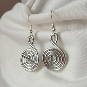 Op de afbeelding: Een paar zilverkleurige spiraalvormige oorbellen. Elke oorbel heeft een opgerold ontwerp, met een haakje voor gemakkelijk dragen. De oorbellen worden getoond tegen een witte stoffen achtergrond, wat hun metallic glans benadrukt. Deze oorbellen zijn een stijlvol accessoire.