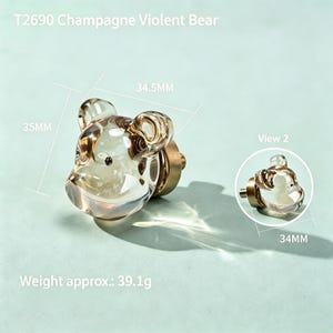 Peut inclure: Un bouton de meuble T2690 Champagne Violent Bear en verre transparent teinté champagne en forme de tête d'ours avec une base en métal doré. Le bouton mesure 35mm sur 34,5mm, avec une vue secondaire de 34mm de large et un poids de 39,1g.