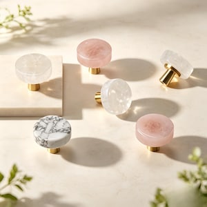 Puede incluir: Un conjunto de seis pomos circulares para armarios con superficies lisas y pulidas en tonos blanco translúcido, rosa suave y un patrón de mármol blanco y gris, cada uno montado sobre una base cilíndrica de metal dorado cepillado.