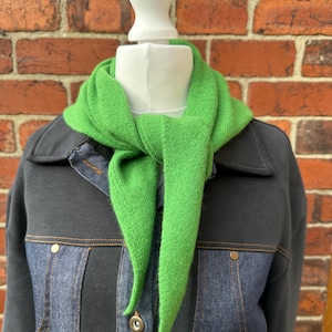 May include: A bright green triangular knit scarf tied around the neck, worn over a dark charcoal grey jacket featuring denim-like panels, a collared neckline, and metallic buttons down the front placket, displayed on a white mannequin torso.