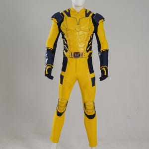 May include: A full-body yellow and navy blue tactical suit featuring molded chest armor, shoulder pads, and knee guards. The ensemble includes long sleeves, matching trousers, and a belt with a central X-shaped buckle emblem at the waist.