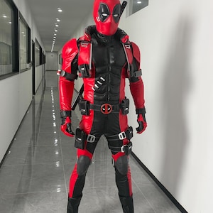 Könnte beinhalten: Ein Deadpool-Ganzkörperkostüm bestehend aus einem strukturierten rot-schwarzen Anzug mit passender Maske. Das Outfit umfasst integrierte Schulterpanzer, einen Gürtel mit runder Schnalle, mehrere aufgesetzte Taschen, Knieschoner und schwarze Stiefel.